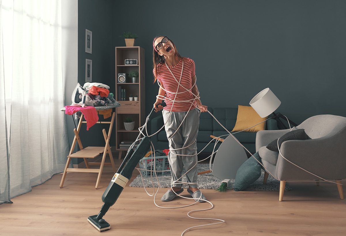 Frustrated housewife doing household chores at home: she is wrapped in cables, screaming and cleaning up a messy room